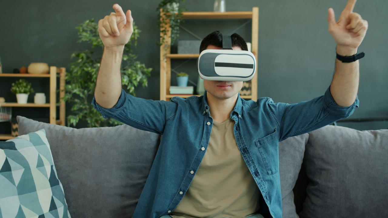 Man wearing vr headset on couch with hands raised