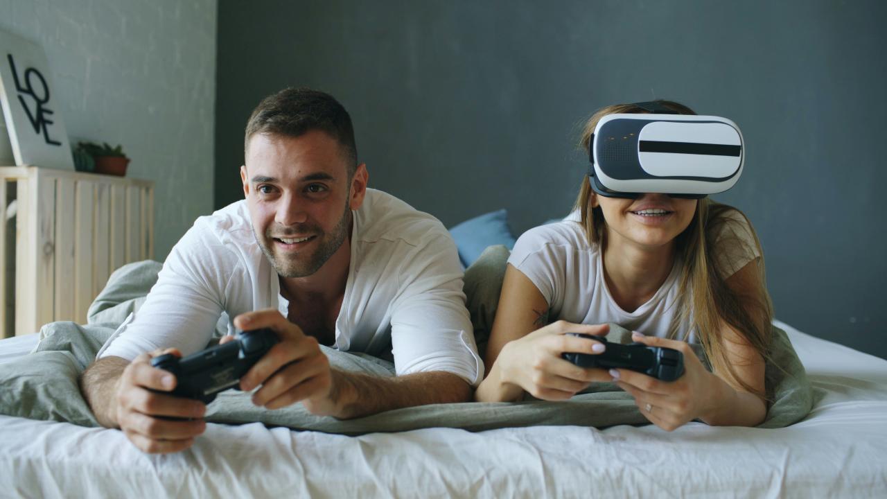 Couple playing video games with vr headset on bed